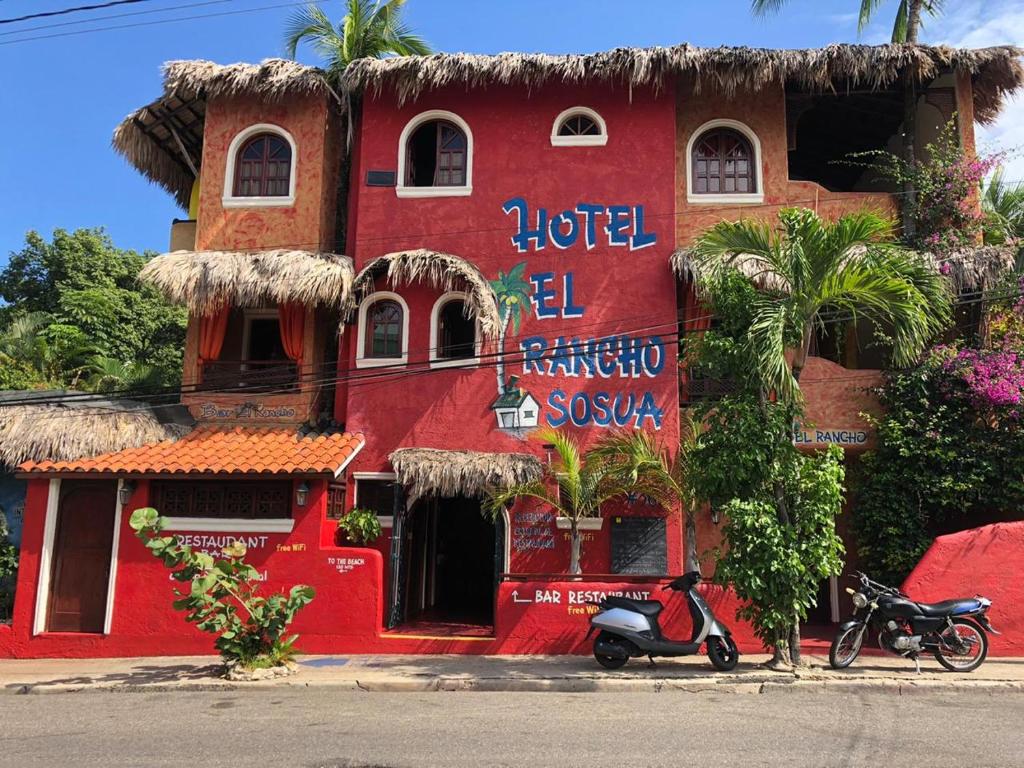 a red building with a scooter parked in front of it at Hotel El Rancho Sosua in Sos&uacute;a
