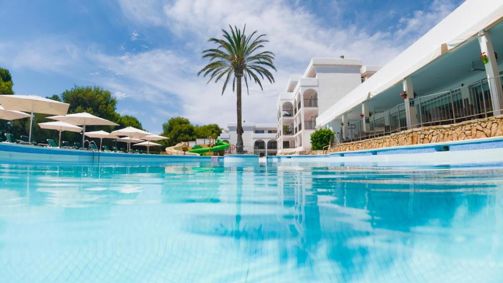 une piscine d'eau bleue en face d'un hôtel dans l'établissement Apartamentos Cala d'Or Playa, à Cala d´Or