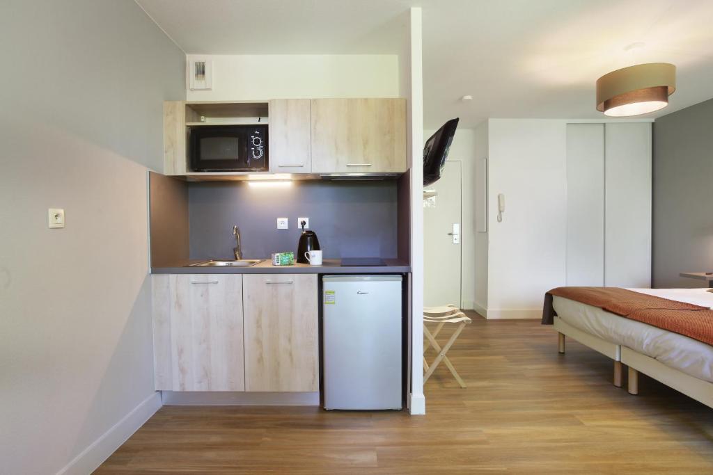 a kitchen with a refrigerator and a bed in a room at Odalys City Aix en Provence Le Clos de la Chartreuse in Aix-en-Provence