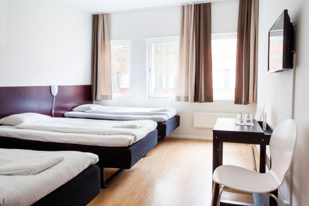 Zimmer mit 3 Betten, einem Tisch und einem Stuhl in der Unterkunft Hotell Dialog in Stockholm