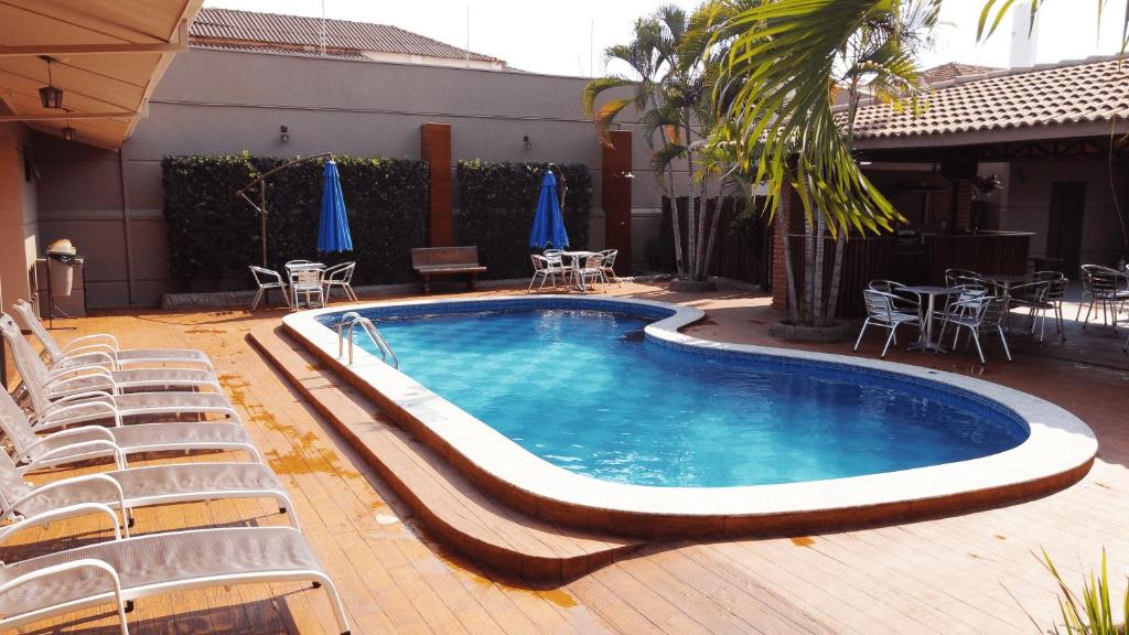 a swimming pool with chairs and tables and umbrellas at Pousada Kaluanã in Olímpia