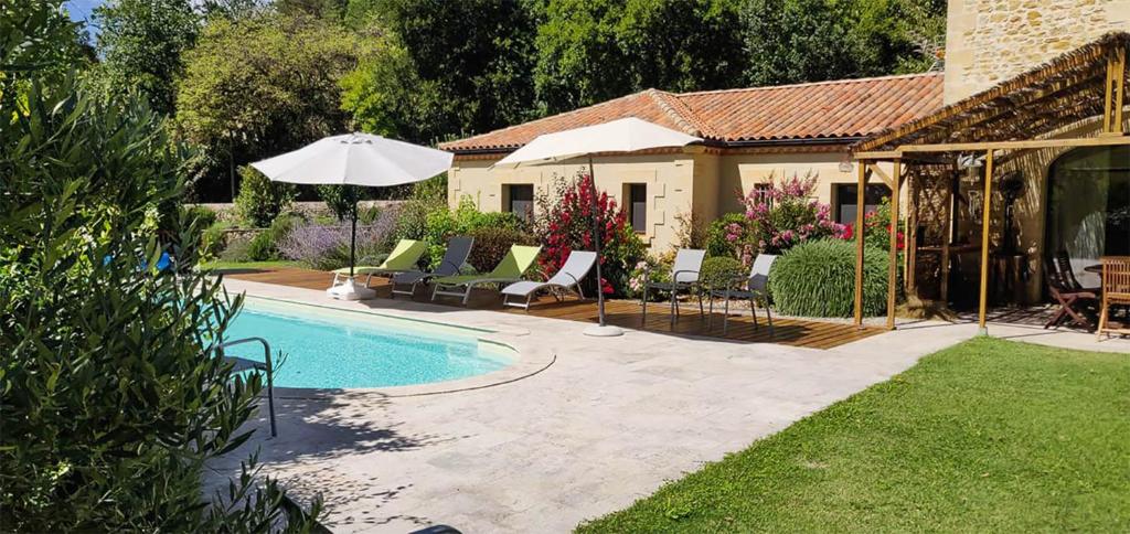 a backyard with a pool with chairs and an umbrella at Le Hibou Heureux in Bézenac