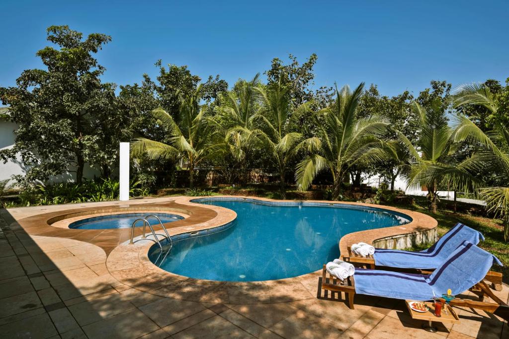 - une piscine avec 2 chaises longues à côté dans l'établissement The Fern Samali Resort, à Dapoli