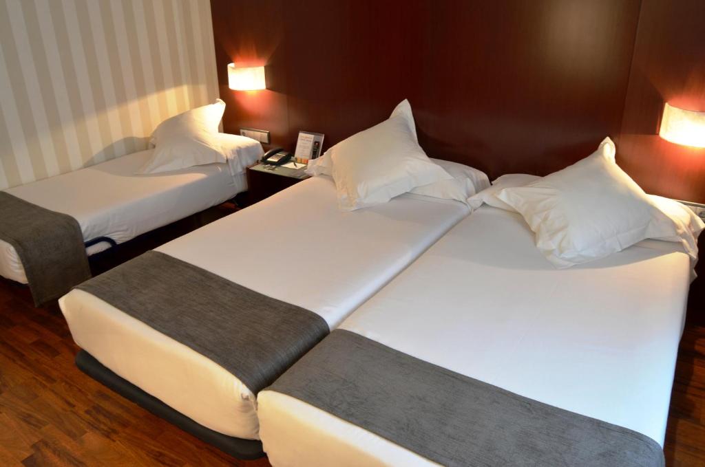 two beds in a hotel room with white pillows at Zenit Málaga in Málaga