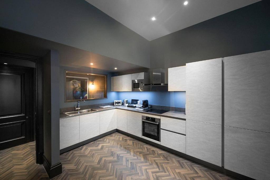 a kitchen with white cabinets and a wooden floor at The Bells - Luxury Serviced Apartments in Leeds