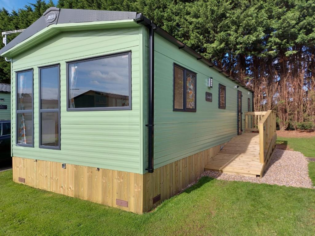 een groen tiny house met een houten terras bij Rustling Pines at Knaresborough Lido in Harrogate