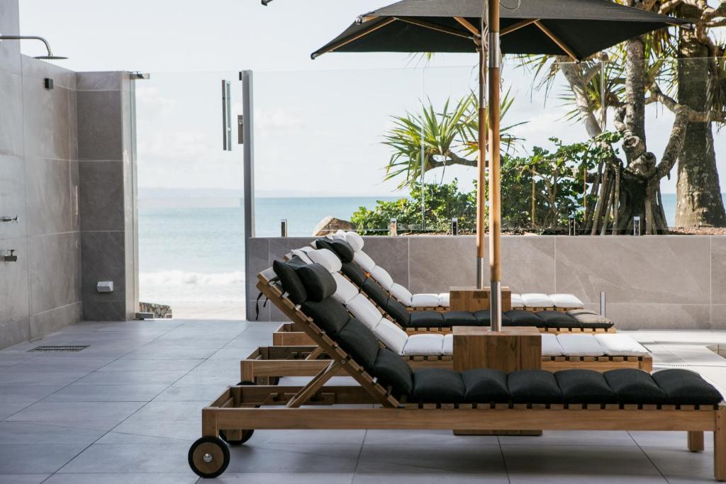 a row of lounge chairs with an umbrella and the ocean at On The Beach Noosa Resort in Noosa Heads