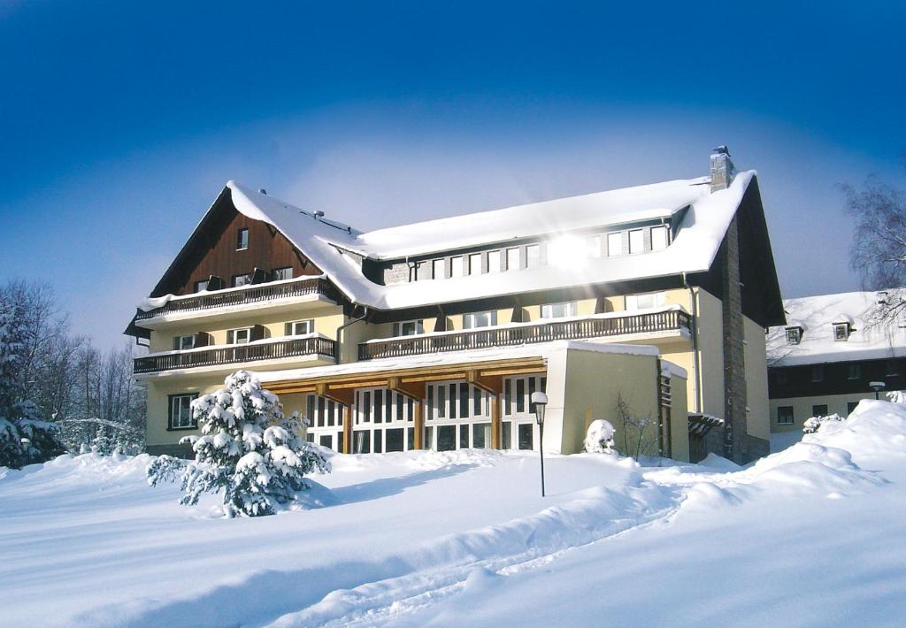 un gran edificio con nieve en el suelo delante de él en Hotel Haus am Ahorn, en Schöneck