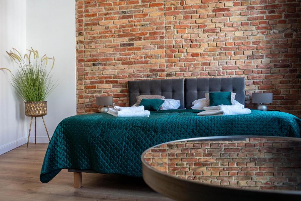 a bed with a green blanket and a brick wall at Kamienica1899 in Szczecin