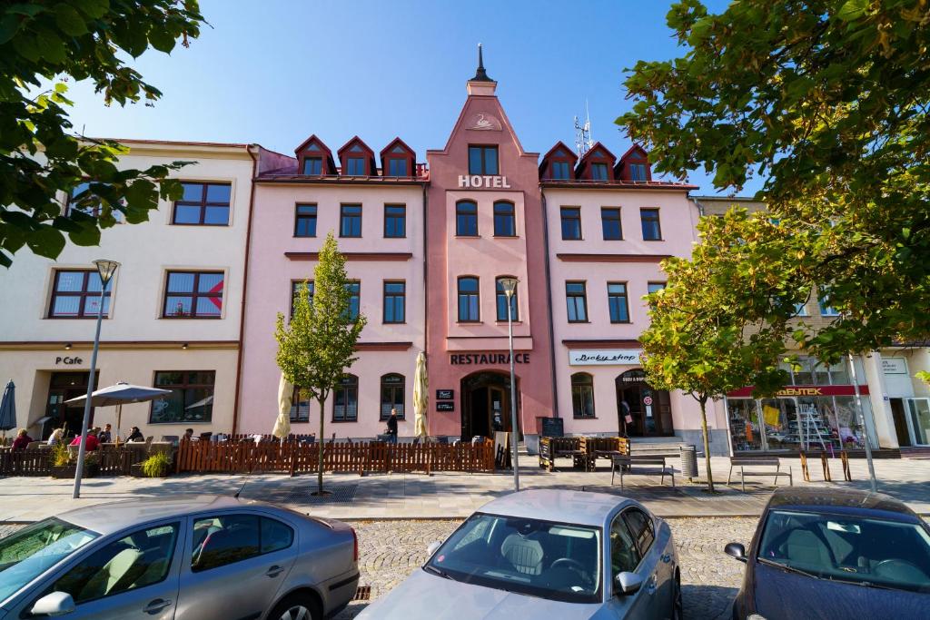 a pink building with cars parked in front of it at Hotel U Labutě in Žďár nad Sázavou