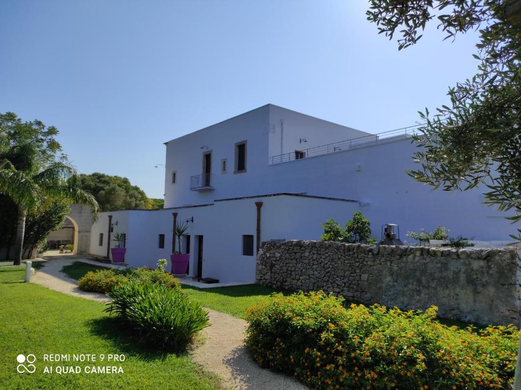 a white building with a stone wall next to a yard at Masseria Borgo Santuri in Ostuni
