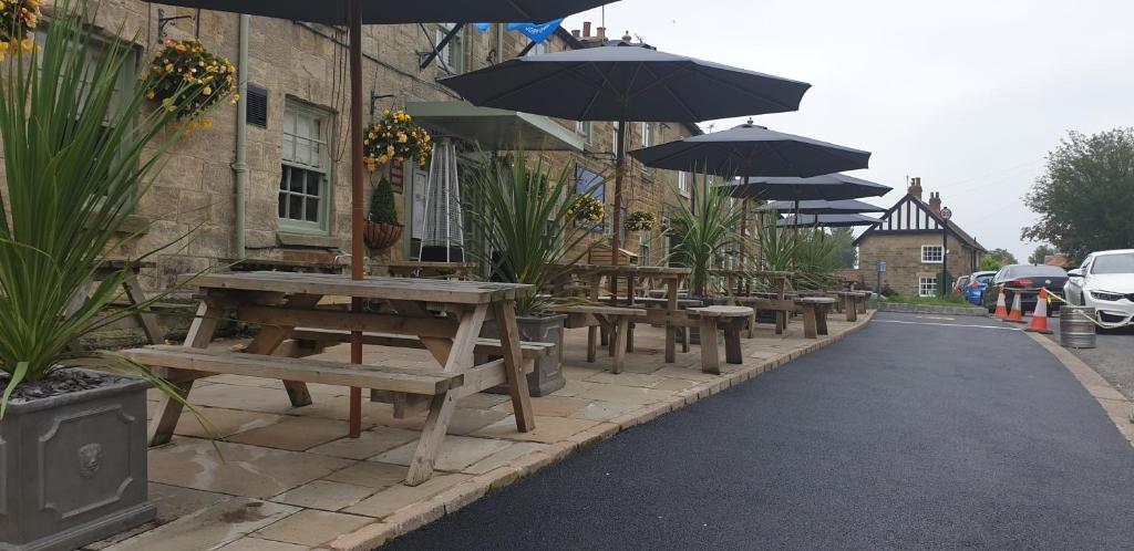 a row of tables and benches with umbrellas on a street at The Queen Catherine Hotel in Osmotherley