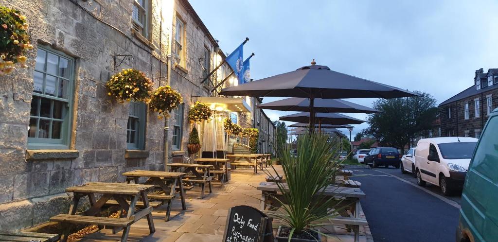a row of tables and benches with an umbrella on a street at The Queen Catherine Hotel in Osmotherley