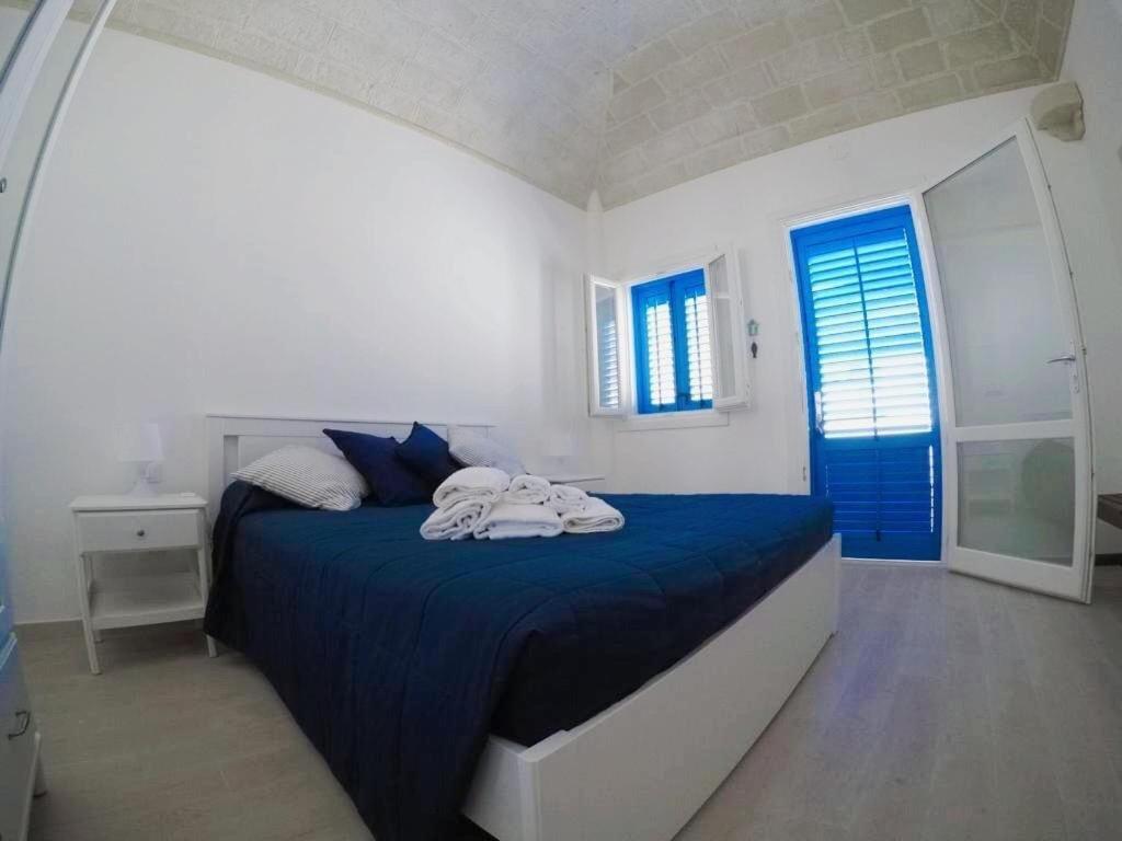 a white bedroom with a blue bed and a window at La Casa del Purpaiolo in Favignana