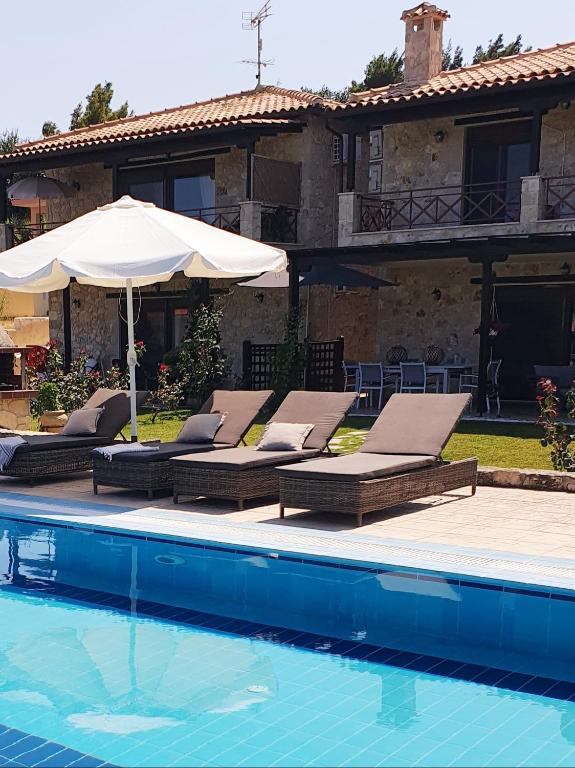 a pool with chairs and an umbrella and a house at Villa Sandra in Kriopigi