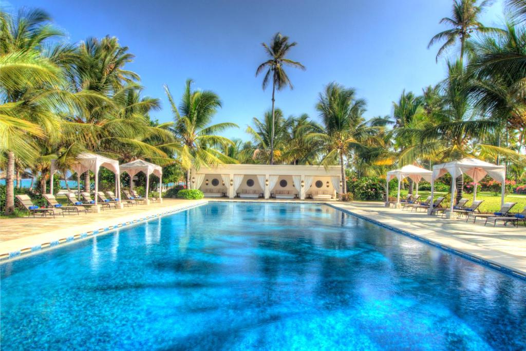 a swimming pool in front of a resort with palm trees at Baraza Resort and Spa Zanzibar in Bwejuu