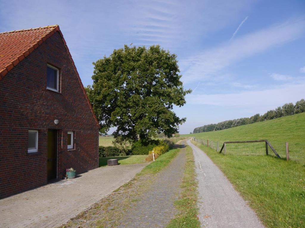 a dirt road next to a brick building and a tree at Ferienhaus am Nordseedeich in Alleinlage in Hooksiel