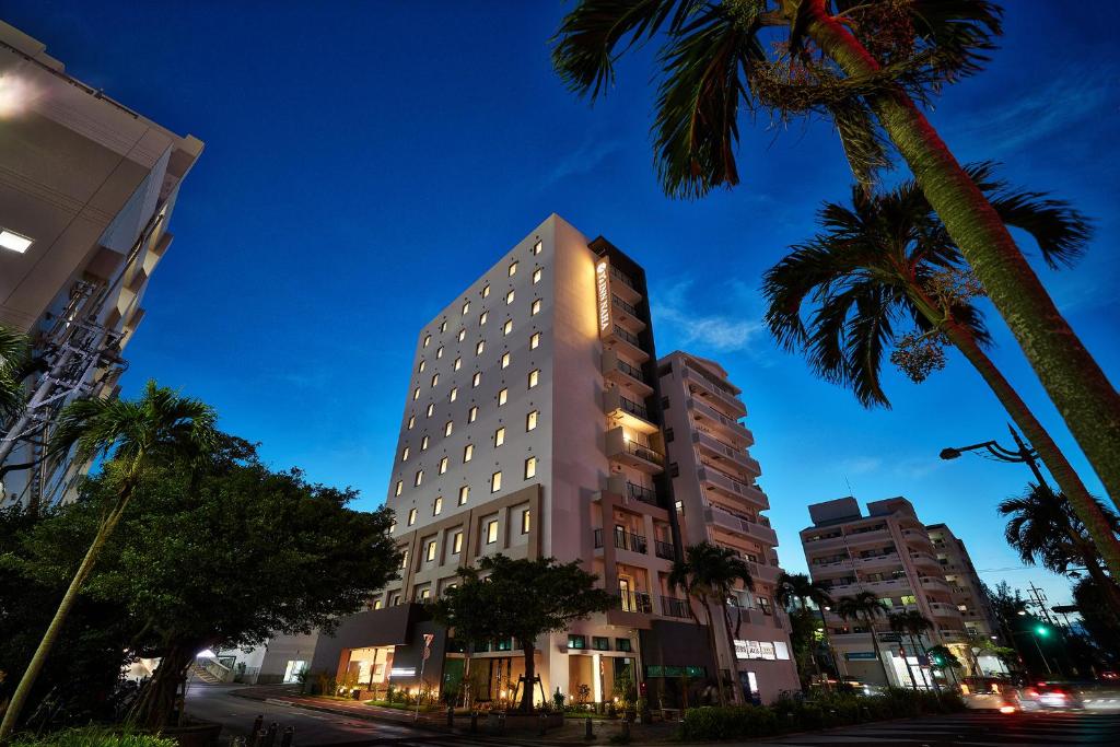 a tall building on a city street with palm trees at Y's Inn Naha Oroku Ekimae in Naha