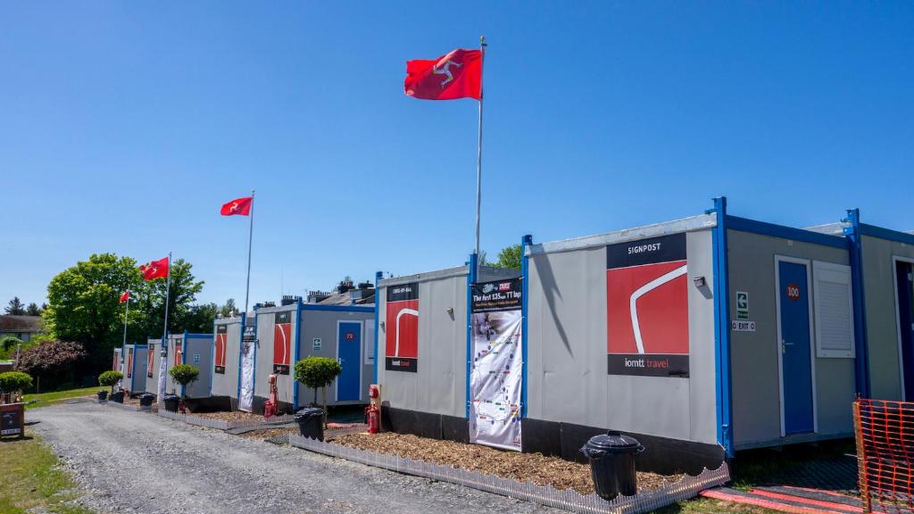 a row of portable toilets on a street with two flags at IOMTT Village at Isle of Man TT in Douglas