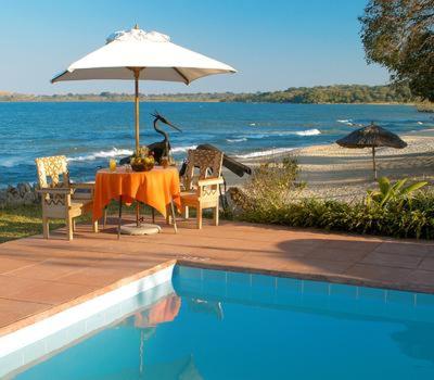 einen Tisch mit einem Sonnenschirm und Stühlen am Meer in der Unterkunft Sunbird Chintheche in Nkhata Bay