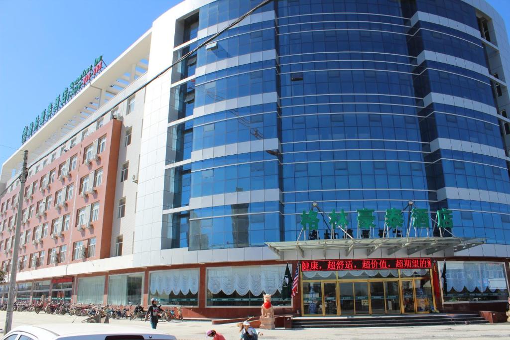 un edificio de cristal alto con gente caminando delante de él en GreenTree Inn Zhangjiakou Yu County Bus Station Business Hotel, en Xiaowa