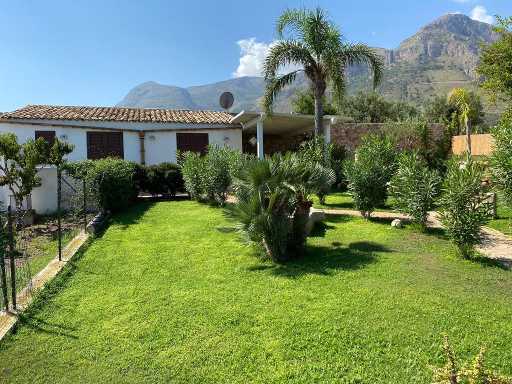 a yard with palm trees and a house with mountains in the background at Villetta Degli Oleandri in Castellammare del Golfo
