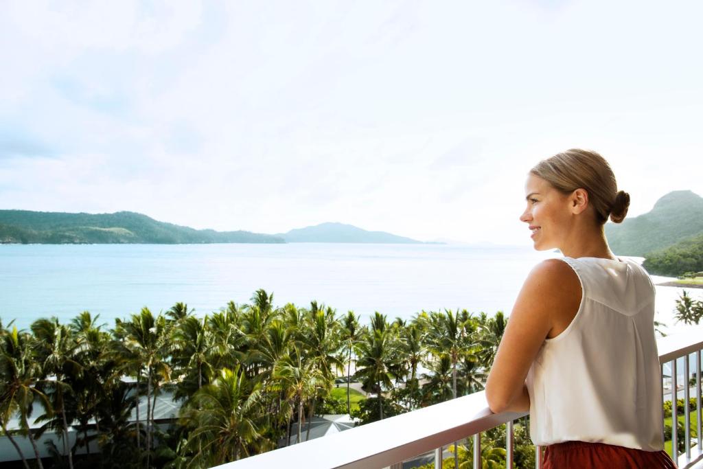 Una mujer parada en un balcón con vistas al agua en Reef View Hotel, en Hamilton Island