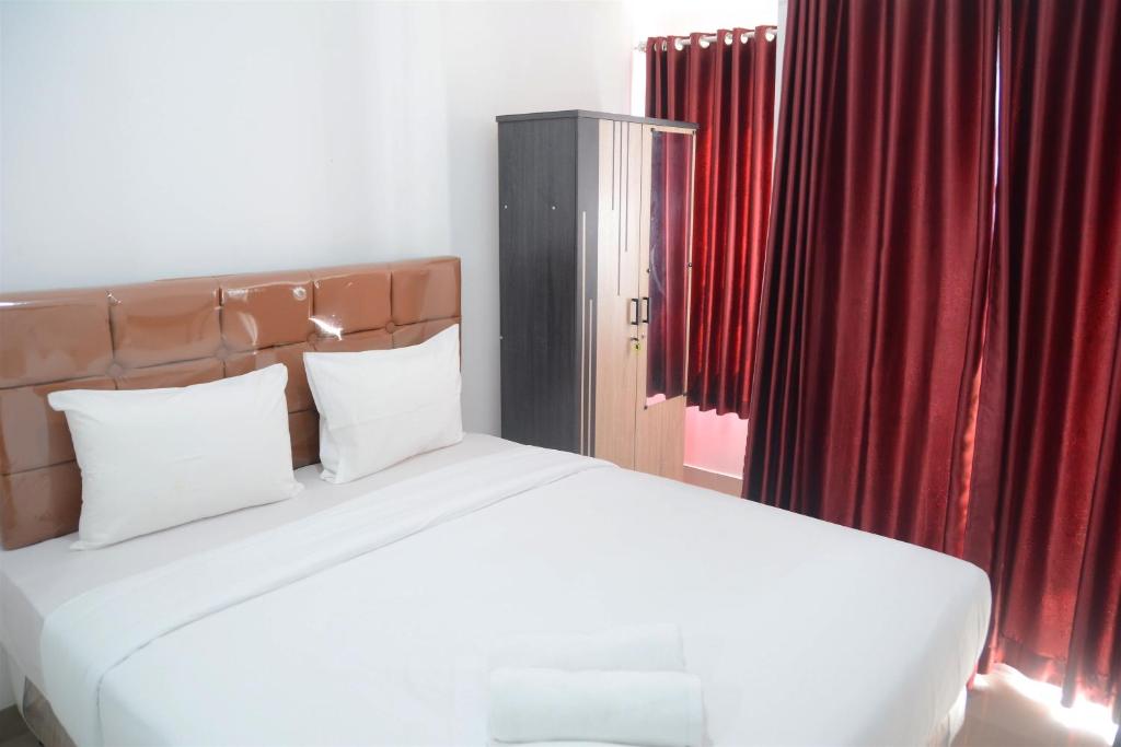 a bedroom with a large white bed with red curtains at Comfy Studio Poris 88 Apartment By Travelio in Poris-lor