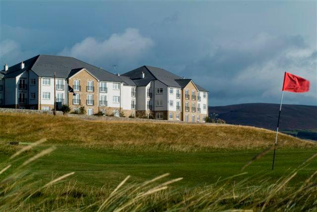a red flag on a golf course in front of a building at Links Apartment in Brora