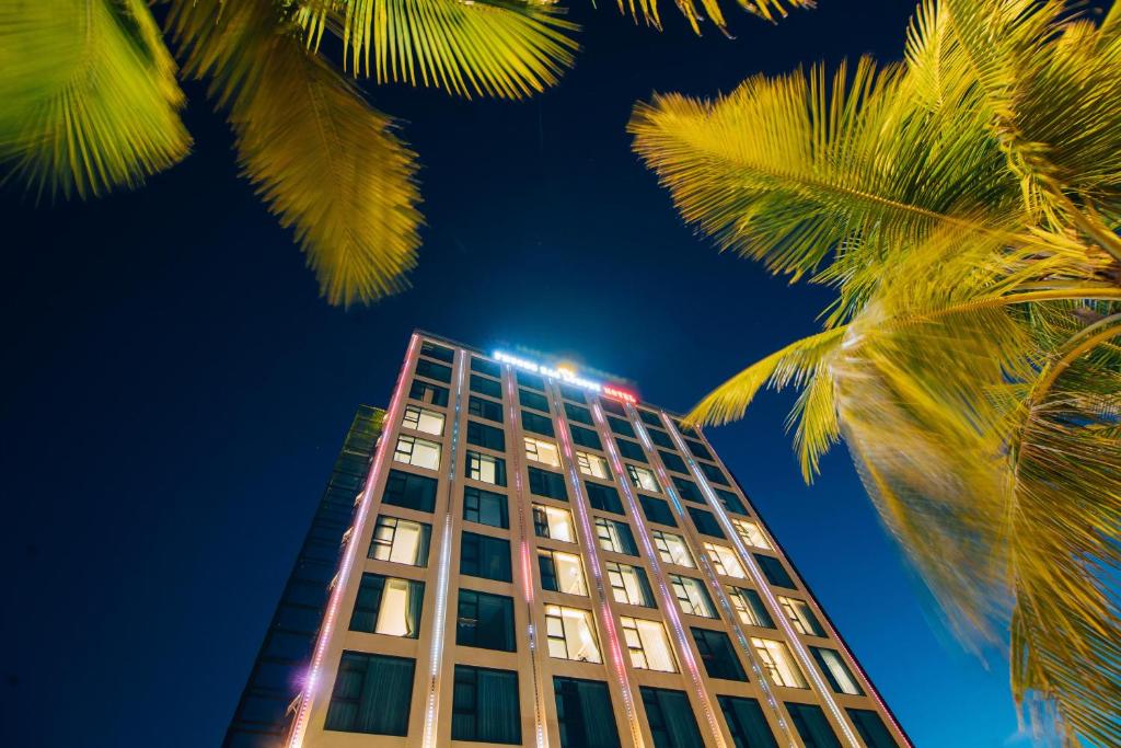 a tall building with palm trees in front of it at Phương Bắc Luxury Hotel in Dong Hoi