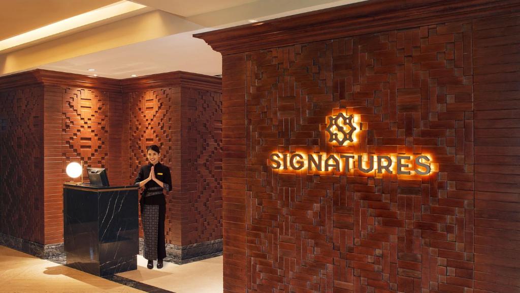 a woman standing next to a brick wall with a sign at Hotel Indonesia Kempinski Jakarta in Jakarta