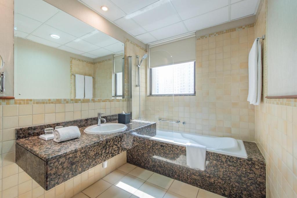 ein Badezimmer mit einem Waschbecken, einer Badewanne und einem Spiegel in der Unterkunft Suha JBR Hotel Apartments in Dubai