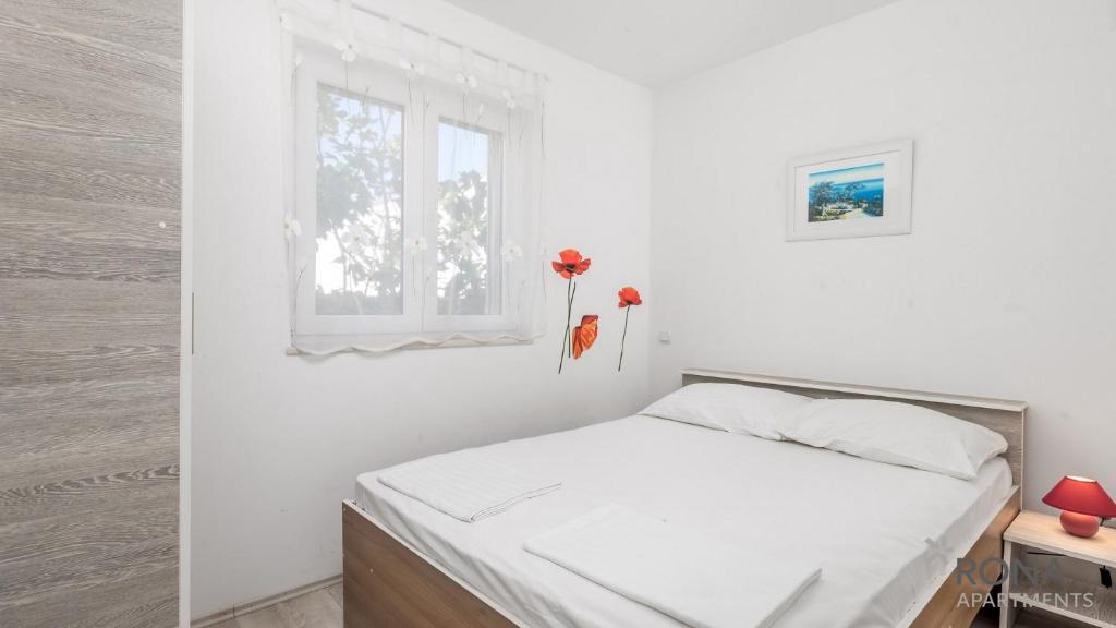 a white bedroom with a bed and a window at Rona Apartments Zlatko in Šimuni