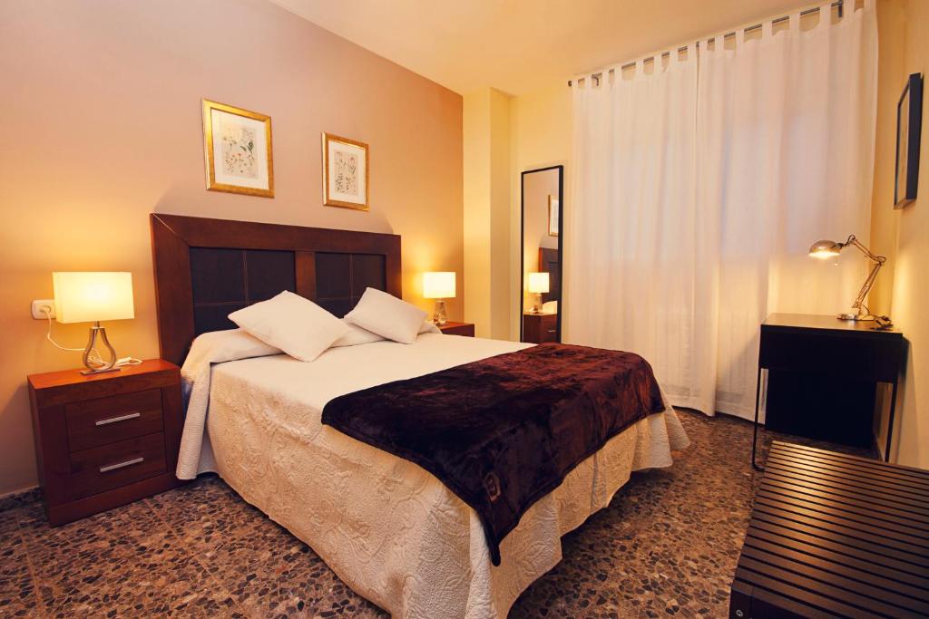 a bedroom with a large bed with two lamps and a window at Apartamentos Turísticos Ceres in Mérida