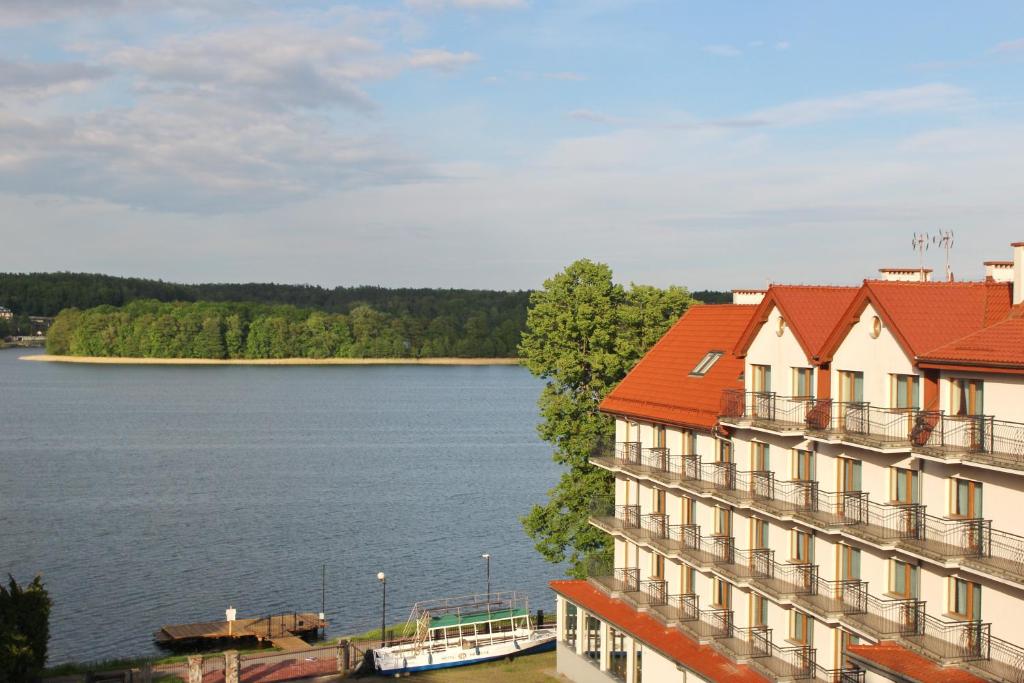 um edifício com um telhado vermelho ao lado de uma massa de água em Hotel Huszcza em Mrągowo