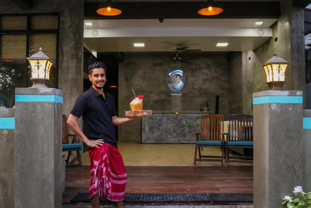 un hombre sosteniendo una bandeja con una bebida en un restaurante en The Mureed, en Fulidhoo