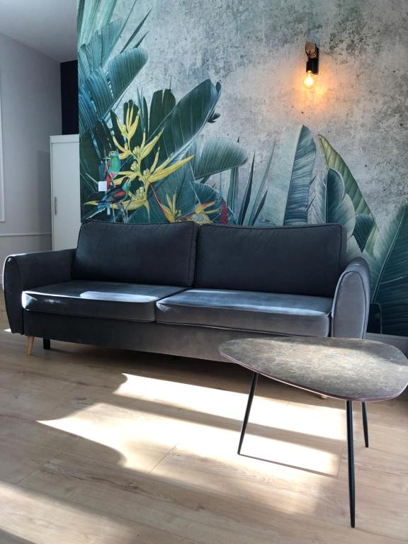 a black couch in a living room with a plant mural at Ara Apartament I in Toruń