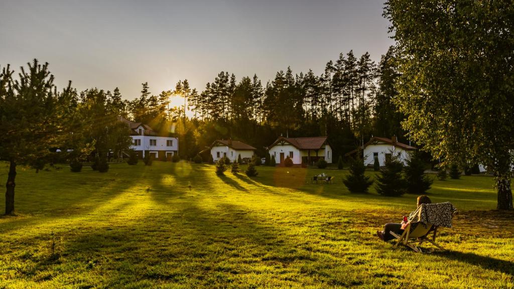 una mujer sentada en una silla en un campo con casas en Gospodarstwo Agroturystyczne Zacisze, en Ruś