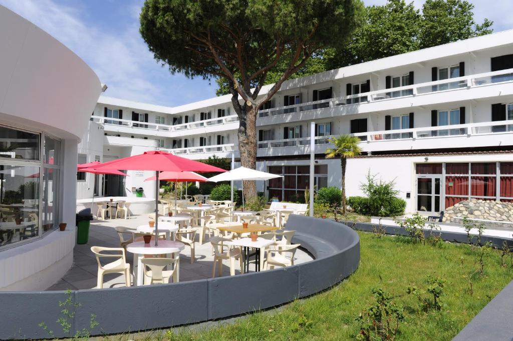 un patio avec des tables et des parasols en face d'un bâtiment dans l'établissement Actif Residence, à La Grande Motte