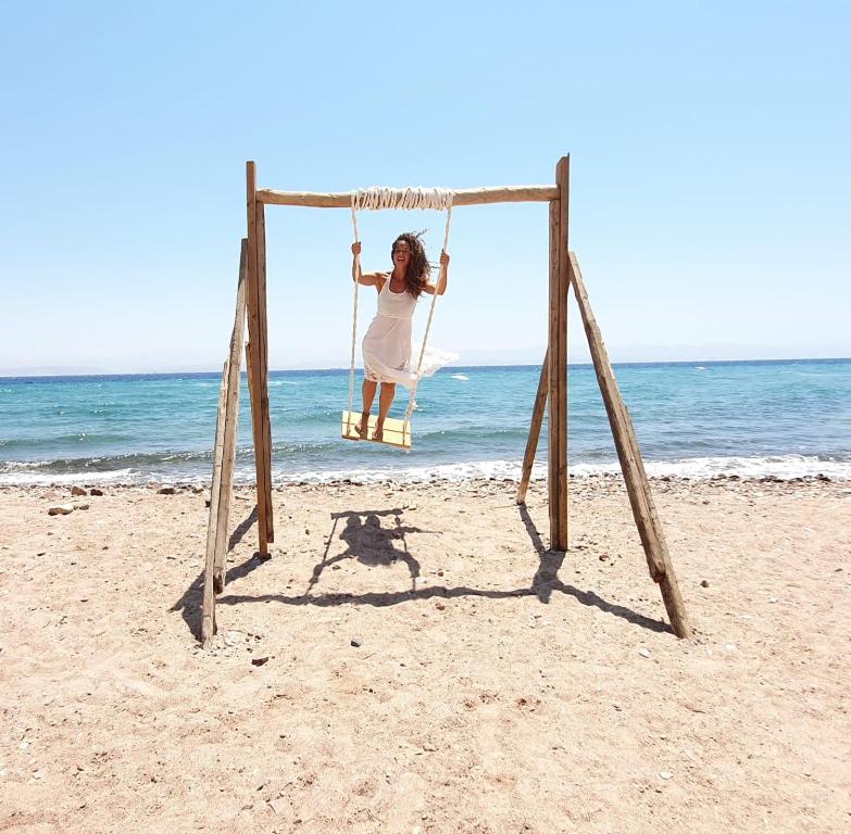 a woman sitting on a swing on the beach at SakraTah Camp - eco friendly in Taba