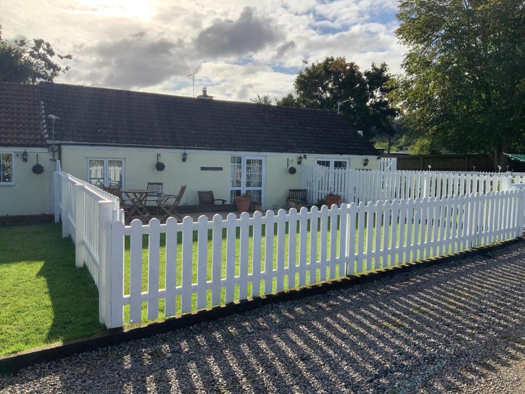 una cerca blanca frente a una casa blanca en woodpecker cottage at frog trotters cottages en Hartpury