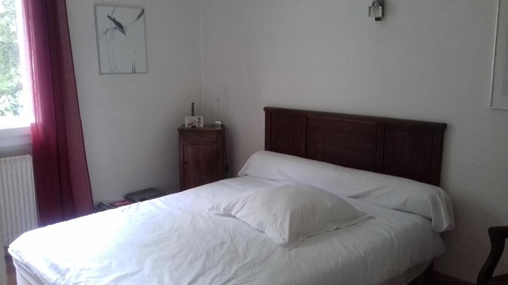 a bed with white sheets and a wooden headboard in a bedroom at chez sylvette in Quinsac