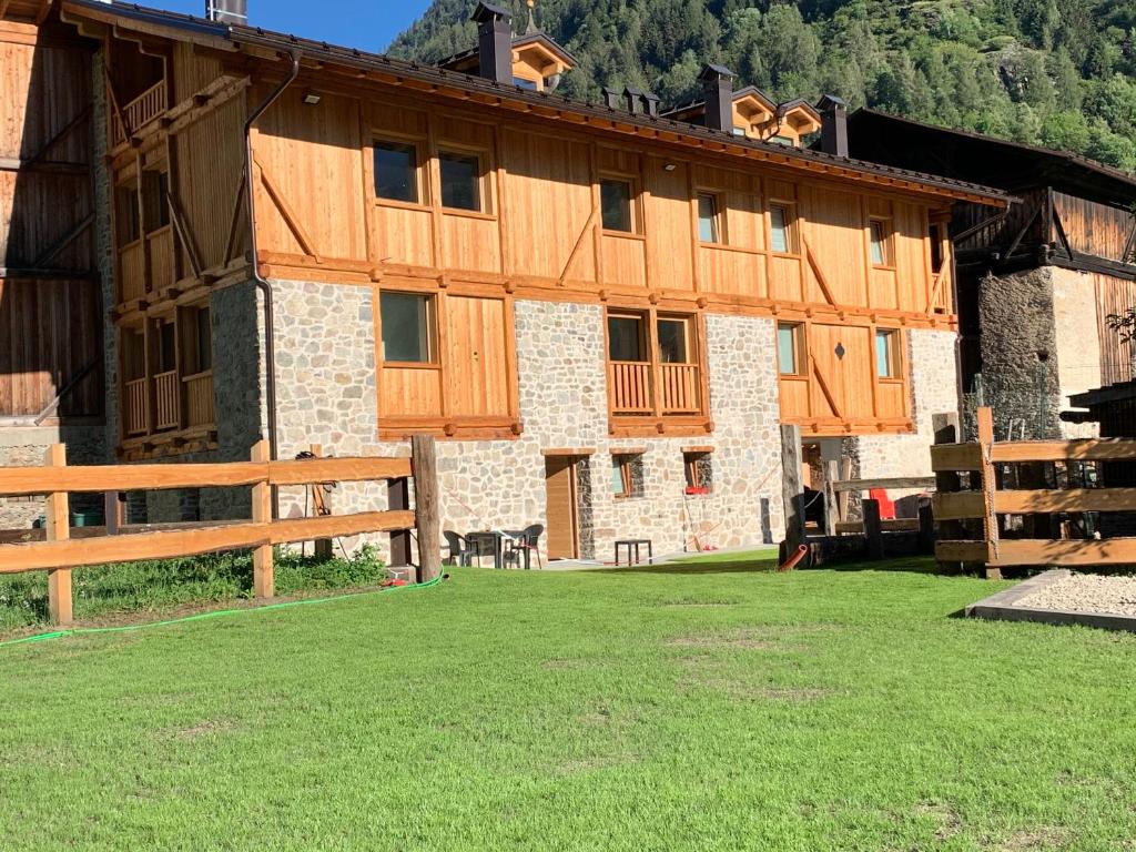 un gran edificio de madera con un campo de césped delante de él en Camelot Luxury Houses Horses en Pellizzano