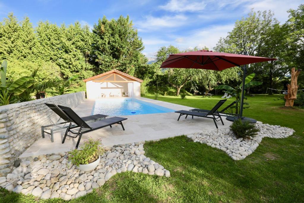un patio con 2 sillas y una sombrilla junto a la piscina en Le Domaine Loft - Piscine - Jacuzzi - Parc en Tullins