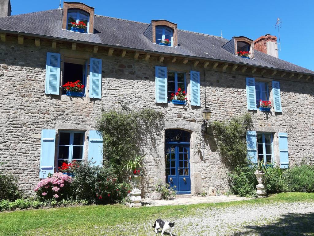 una casa de piedra con persianas azules y flores en las ventanas en Manoir de la Peignie, en Merdrignac