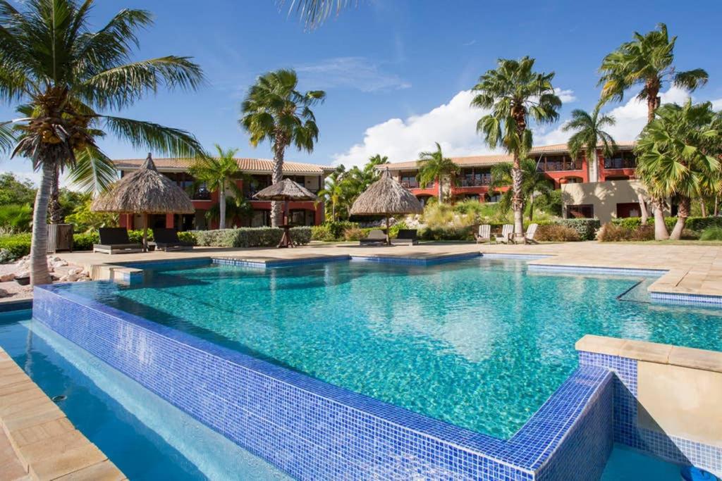 a swimming pool in front of a resort with palm trees at Spanish Water A1 in Willemstad