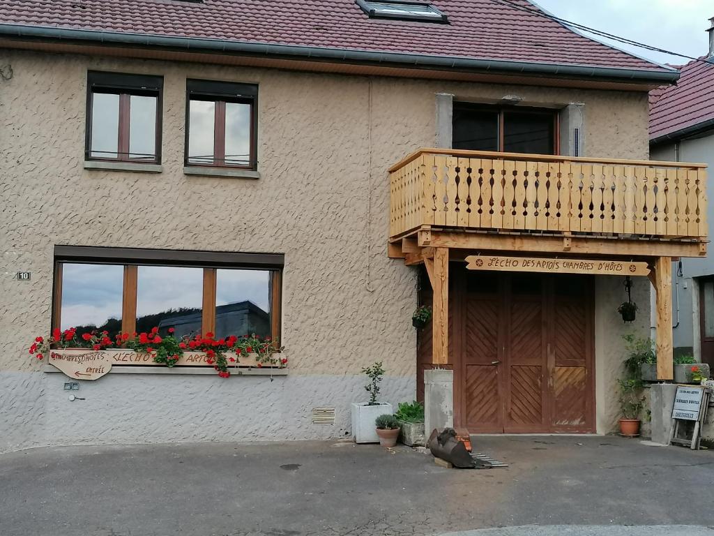 un chien assis devant une maison avec balcon dans l'établissement L'écho des Artois, à Uzelle