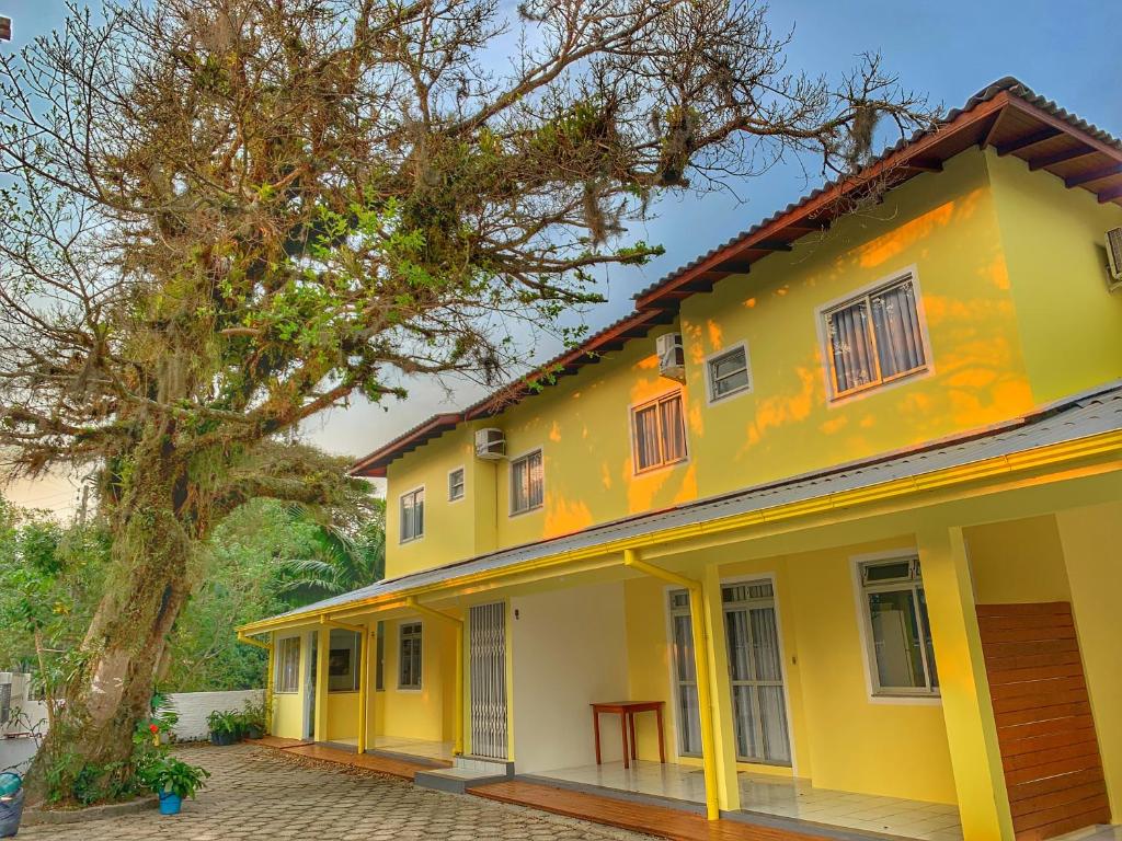 een geel huis met een boom ernaast bij Pousada Figueira in Guarda do Embaú