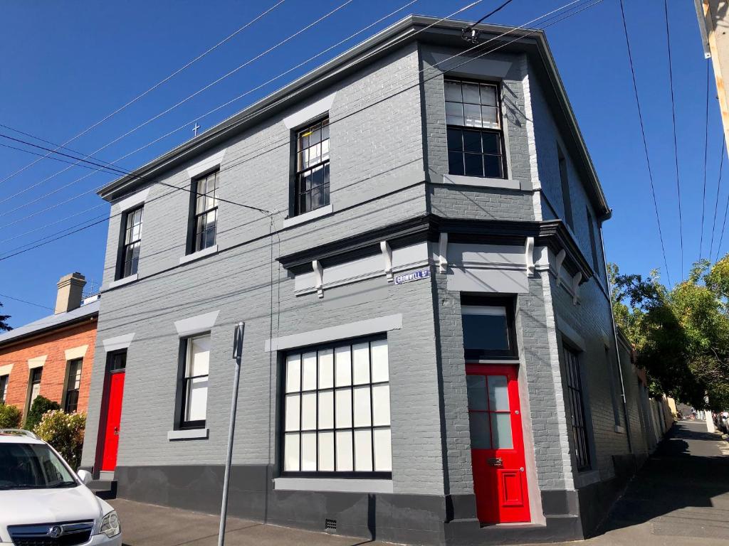 a gray house with a red door on a street at Cromwell Apartment - 3 Red Doors Battery Point in Hobart