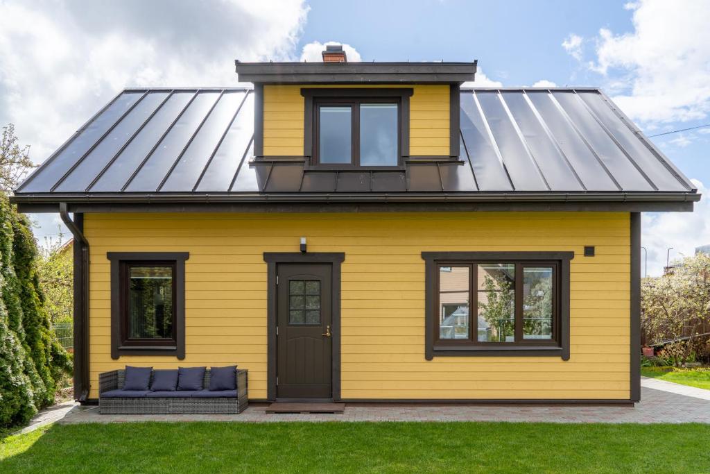a yellow house with a black roof at Cosy Family Guesthouse with Sauna and Garden in Kuressaare